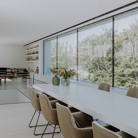 Spacious, minimalist dining area with floor-to-ceiling glass walls offering scenic forest views.