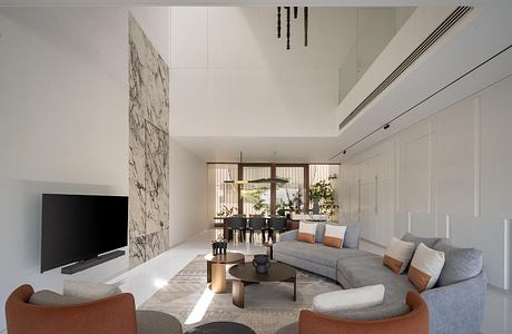 Spacious modern living room with minimalist furniture, marble wall accent, and abundant natural light.