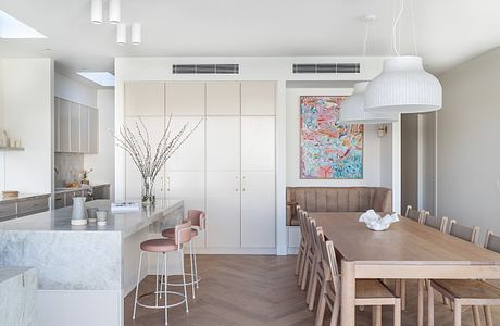 Modern kitchen and dining area with sleek white cabinets, colorful artwork, and stylish furnishings.