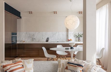 Sleek, modern kitchen with white marble backsplash, wood cabinetry, and round pendant light.