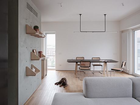 Modern, minimalist apartment with light wood shelves, neutral furniture, and a dog.
