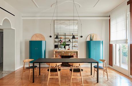 Sleek modernist dining room with bold turquoise cabinets, arched shelving, and statement chandelier.