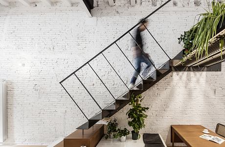 An open-concept interior with a modern steel staircase, wooden furniture, and brick walls.