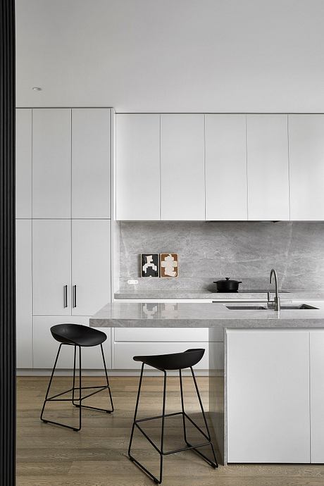 Modern minimalist kitchen with sleek white cabinets, concrete countertops, and black bar stools.