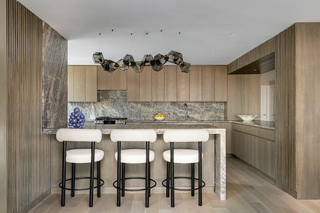 Modern kitchen with sleek gray stone countertop, geometric light fixtures, and white bar stools.