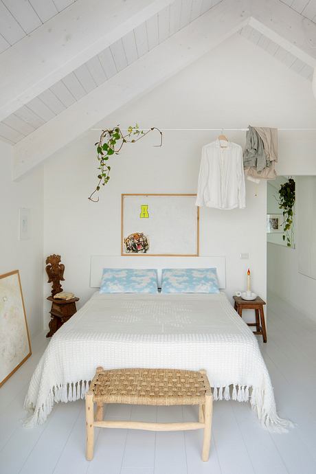 Cozy attic bedroom with white walls, wood accents, and hanging plants creating a serene atmosphere.