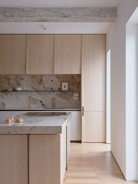 A minimalist kitchen with wood cabinetry, marble countertops, and a sleek backsplash.
