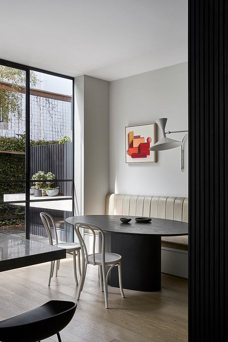 Contemporary dining area with sleek black table, vintage-style chairs, and vibrant abstract artwork.