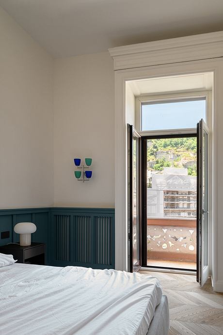 Spacious bedroom with wood-paneled wall, glass doors leading to balcony, and decorative sconce.