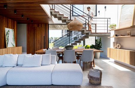 Modern, open-concept living space with wooden accents, hanging light fixture, and glass staircase.