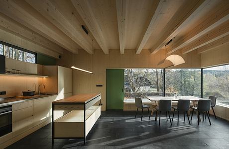 A modern, open-concept kitchen and dining room with exposed wooden beams and large windows.