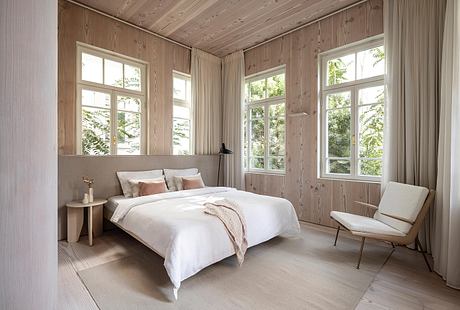 Cozy wood-paneled bedroom with large windows showcasing serene nature views.