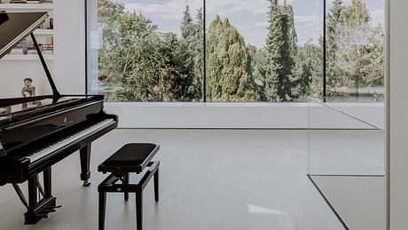 Modern piano room with expansive glass walls and lush outdoor views.