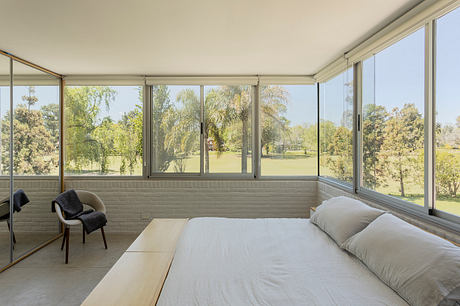 Spacious bedroom with floor-to-ceiling windows showcasing lush outdoor views. Minimalist decor.