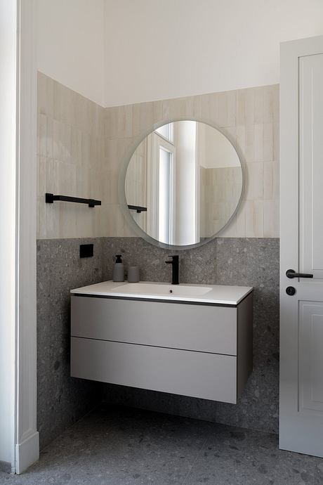 Minimalist bathroom with a circular mirror, floating vanity, and gray tile walls.