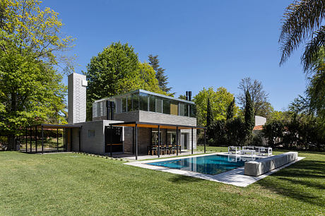 Modern two-story house with glass walls, pool, and lush green surroundings.