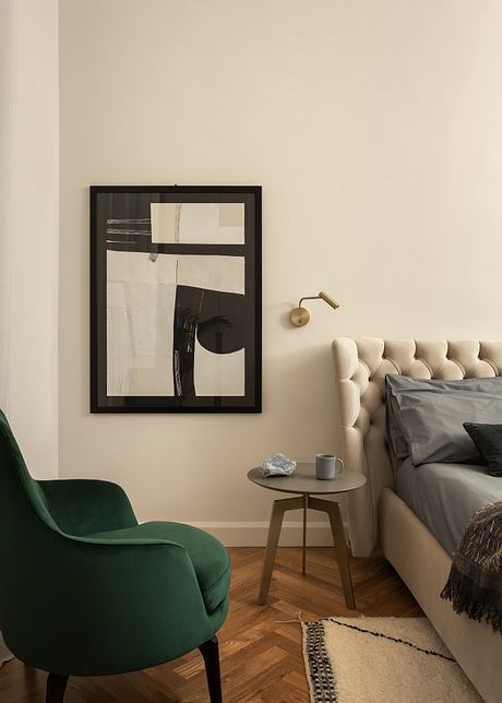 Cozy bedroom with a tufted headboard, green velvet chair, and abstract wall art.