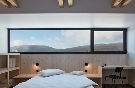 Large windows offer panoramic mountain views in this modern, wood-paneled bedroom.