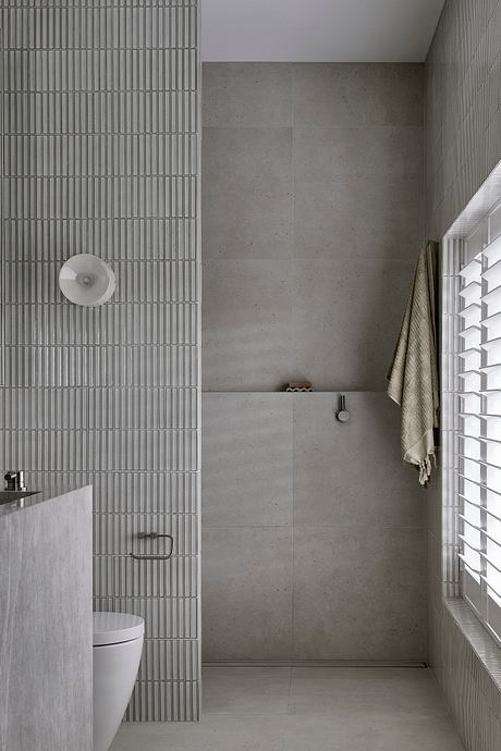 Modern bathroom with minimalist concrete and wire mesh tiles, recessed lighting, and a towel hanging on the wall.