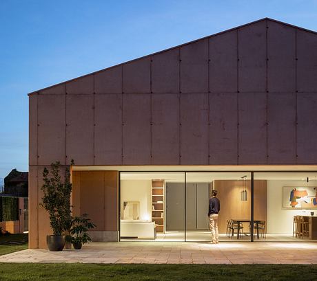 A modern, minimalist house with a distinctive dark exterior and large glass windows showcasing the interior.