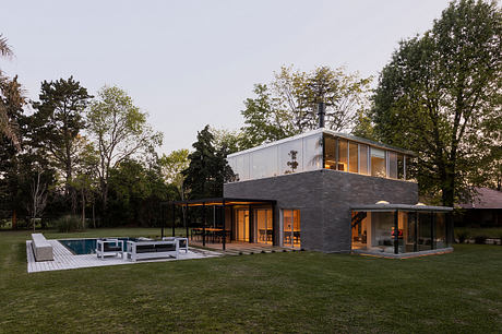 Modern home with sleek design, large windows, and a pool in a lush, wooded setting.