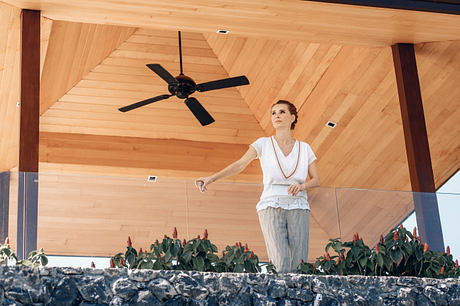 Wooden ceiling with ceiling fan, potted plants, and stone wall create a cozy, rustic ambiance.