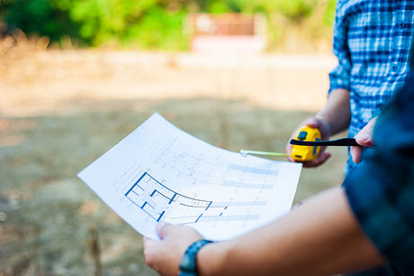 Blueprint plans held in person's hands against natural outdoor setting.