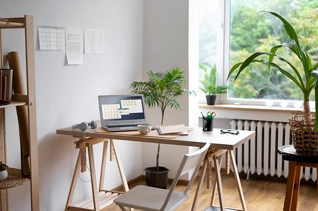 Cozy, plant-filled home workspace with wooden desk and large window overlooking greenery.