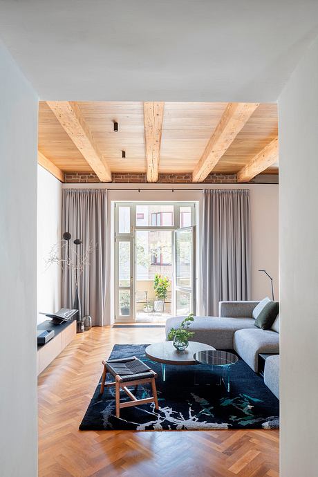 Modern living room with exposed wood beams, large windows, and a plush area rug.