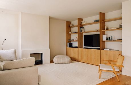 Minimalist living room with warm wood shelving, fireplace, and cozy furnishings.