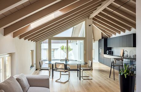 Spacious open-plan living area with exposed wooden beams, large windows, and modern furnishings.