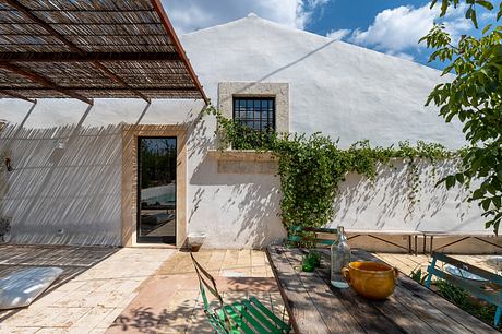 Rustic exterior with thatched roof, concrete window frame, and lush greenery surroundings.