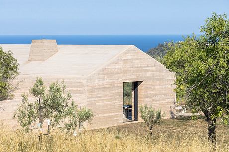 A modern, minimalist concrete house with a striking roofline and large windows overlooking the sea.