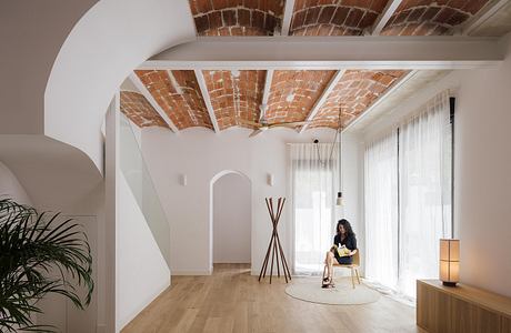 Spacious room with arched brick ceiling, wood floors, and a woman relaxing on a chair.