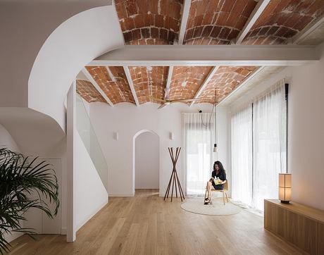 Spacious room with arched brick ceiling, wood floors, and a woman relaxing on a chair.