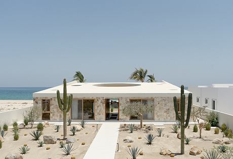 Modern desert-style home with stone facade, cactus landscaping, and ocean view.