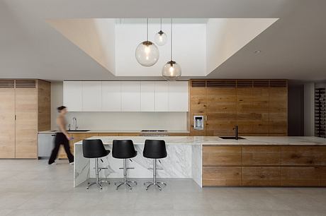 Sleek, modern kitchen with white cabinetry, wood accents, marble island, and globe pendant lights.