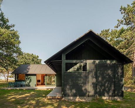 A modern, rustic cabin nestled in a wooded setting with a wraparound porch and clean lines.