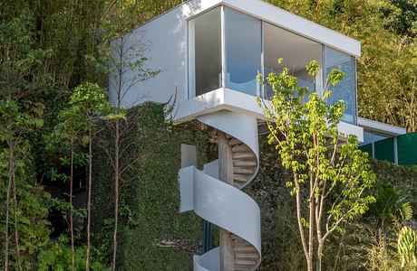 A modern, glass-enclosed structure with a spiral staircase, surrounded by lush greenery.