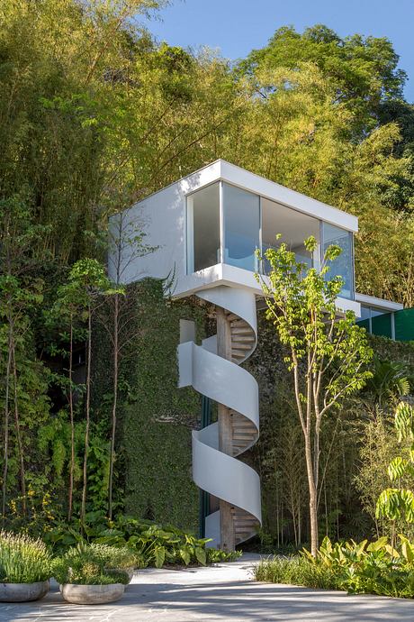 A modern, glass-enclosed structure with a spiral staircase, surrounded by lush greenery.