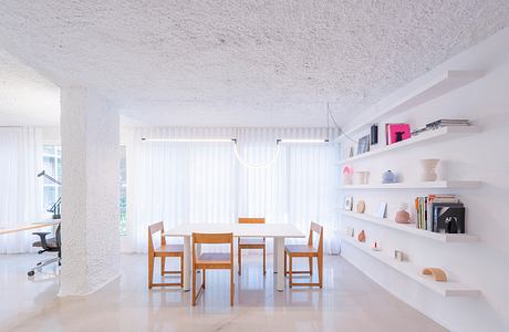 Bright, minimalist dining space with wooden table and chairs, open shelving, and textured ceiling.