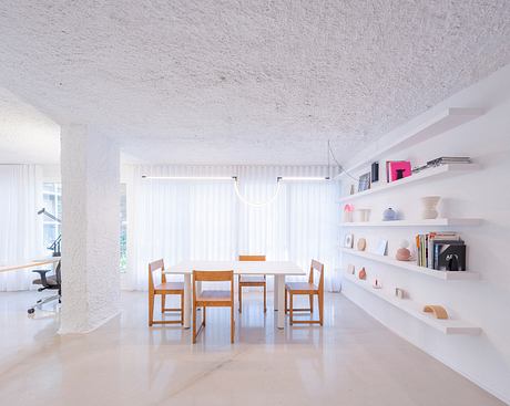 Bright, minimalist dining space with wooden table and chairs, open shelving, and textured ceiling.