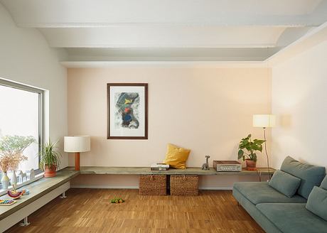 Spacious living room with wooden floors, planter, artwork, sofa, and storage bench.