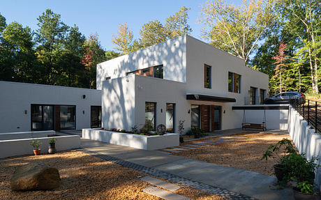 A modern, two-story home with a minimalist exterior, large windows, and a paved walkway leading to the entrance.