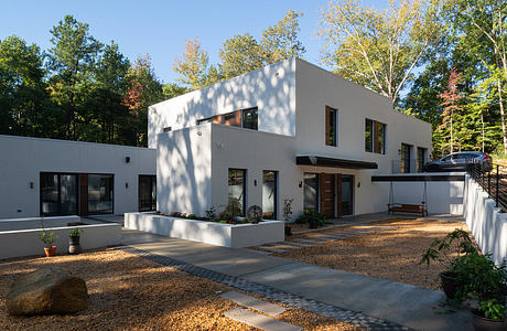 A modern, two-story home with a minimalist exterior, large windows, and a paved walkway leading to the entrance.