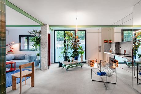 Spacious open-plan interior with concrete floors, plants, and modern furniture. Vibrant color accents.