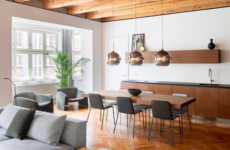 Modern open-plan living space with wooden beams, sleek furniture, and copper pendant lights.