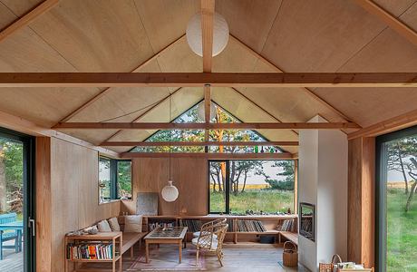 Cozy cabin interior with vaulted wood-paneled ceiling, large windows offering scenic view.