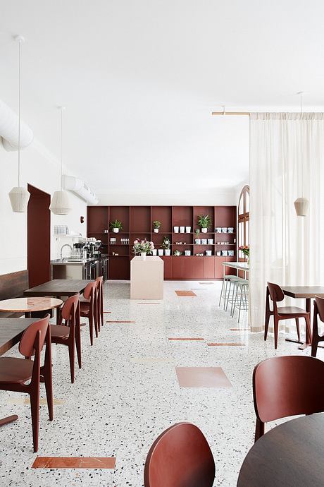 Minimalist cafe interior with burgundy cabinets, terrazzo flooring, and pendant lighting.