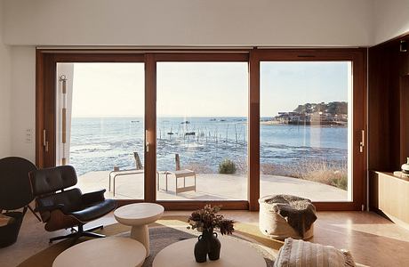 Cozy living space with large windows offering a stunning view of the coastline, featuring minimalist furniture and decor.